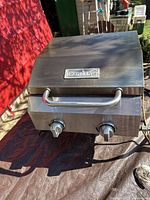 Front view of the portable Nexgrill gas grill showing the lid with handle and two control knobs below. Stainless steel finish with some wear.