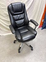Front angled view of the black leather ergonomic office chair showing headrest, padded armrests, and caster wheels.