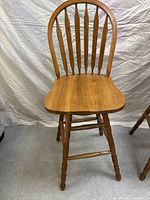 Front view of one oak wooden spindle back bar stool showing the contoured seat, spindle backrest, and turned legs.