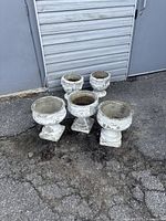 Five white concrete classical outdoor planters arranged on ground near a building. Show overall lot contents and condition.