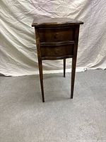 Front view of the vintage wooden side table, showing two curved drawers with wooden knobs and a rectangular top with scalloped edges