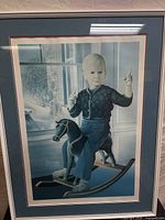 Full view of the framed art print showing a child on a rocking horse inside by a window with a winter scene outside.