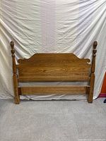 Front view of the oak wood headboard showing turned posts, curved top, and carved design details on the solid wood panel.