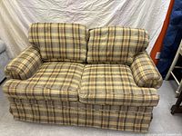Front view of a traditional loveseat with brown and beige plaid fabric upholstery, showing two seat cushions and two back cushions with padded armrests.