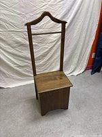 Front view of wooden valet stand showing curved hanger and rectangular box base with hinged top.