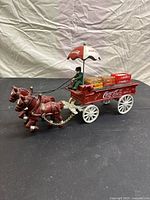 Full view of the Coca-Cola horse-drawn carriage model showing two horses harnessed to the red carriage with white wheels, driver under the umbrella, and miniature Coca-Cola crates on the carriage bed.