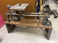 Side view of vintage Shop Smith table saw mounted on metal and wood stand, showing blade, motor, and foot pedal.