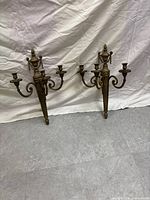 Pair of brass wall-mounted candelabras placed on floor against white backdrop showing full front views