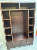 Front and angled view of the dark brown wooden entertainment center showing its open shelves, central compartment for TV, and two drawers with metal pulls.