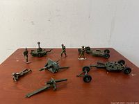 Full view of set showing 4 soldier figures and 6 artillery pieces laid out on wooden surface. One artillery piece missing a wheel as visible.