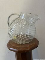 Full side view of the clear ribbed glass pitcher resting on a wooden stool.