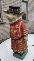 Full view of pig Beefeater resin statue from front showing detailed uniform with gold embroidery, black hat with multi-colored decorations, and green base.