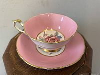 Photo showing the pink teacup with cabbage rose floral design and matching pink saucer with gold trim on a wooden surface