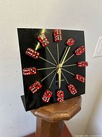 Front angle view of the black square clock with red dice as hour markers on a wooden stand
