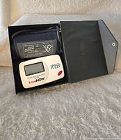 KnowNow digital blood pressure machine with cuff and black protective case, showing LCD screen and red button.