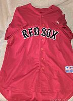 Front of red Boston Red Sox Majestic jersey showing 'RED SOX' lettering and buttons.