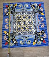 Top-down photo of square blue tablecloth with Portugal and fish pattern with a tape measure showing length about 47 inches