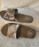 Pair of new men's Realtree slide sandals with camouflage patterned straps and brown footbed.