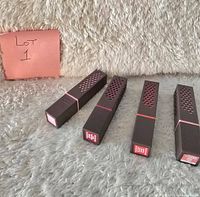 Four Burt's Bees lipsticks in rectangular brown packaging with honeycomb design, placed horizontally on a grey carpet.