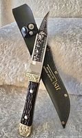 Detailed view of the Bowie knife with engraved blade and decorative handle along with the black leather sheath.