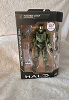 Front view of boxed Master Chief figure sealed in packaging, showing the figure and included accessories inside clear window.