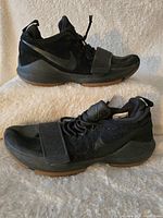 Side view of men's black Nike Paul George basketball shoes with gum sole and lace strap.