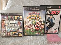 Three video games displayed side by side: Grand Theft Auto V for PS3, Super Monkey Ball 2 for GameCube, NHL 2K7 for PS2.