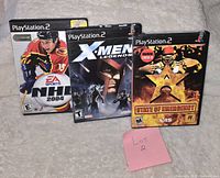 Front view of three PlayStation 2 game cases showing cover art for NHL 2004, X-Men Legends, and State of Emergency with a pink note labeled 'Lot 2'.