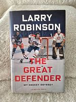 Front cover of the hardcover book 'The Great Defender: My Hockey Odyssey' by Larry Robinson showing three ice hockey players and title text.