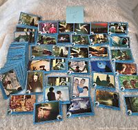 Array of blue-bordered vintage E.T. movie trading cards fanned out and laid display style on soft beige carpet surface, showing various scenes and characters from the movie.