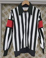 Front view of the black and white vertically striped NHL referee jersey featuring red armbands on sleeves, zipper closure, and solid black collar, cuffs, and hem.