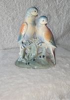 Front view of the ceramic figurine showing two parakeets perched on a branch with leaves and berries.