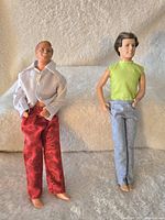 Two vintage Ken dolls posed sitting, one with a white jacket and red pants, the other with a green sleeveless shirt and gray pants