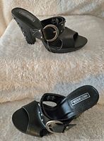 Side view of one black sandal pump showing the open toe, chunky heel and studded detailing with silver buckle.