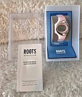 Digital women's ROOTS watch in pink and white in original display box with instruction manual on plush surface.