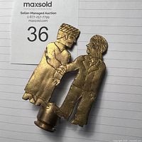 Front angle of brass figurine showing two men shaking hands, attached to a bullet shell base with detailed clothing and facial features.