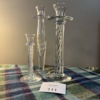Three crystal candlesticks of varying heights displayed together on a plaid blanket with auction lot number.