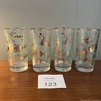 Four clear glass highball glasses with gold and white aquatic fish designs, arranged side by side on a wooden surface.
