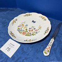 Cake plate and matching knife on blue background, showing floral and butterfly design on plate and matching handle of knife.