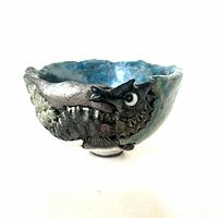 Side angle view of blue-green iridescent raku pottery bowl showing detailed seahorse figure and textured surface.