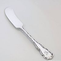 Butter spreader angled showing ornate Louis XV pattern handle with monogram 'F' and flat butterfly blade.