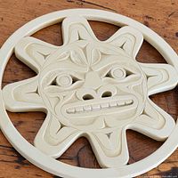 Close-up image showing the detailed stylized sun mask face with carved features and the off-white color of the trivet.