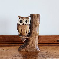 Front view of carved wooden owl perched on tree branch with large contrasting round eyes.