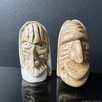 Pair of two small soapstone false face mask carvings on black surface, one light-colored and one tan-colored