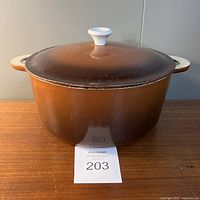 Front view of brown Descoware cast iron enamel pot with lid and cream handles placed on wooden surface.