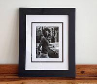 Front view of framed "Windblown Jackie, 1971" photographic print by Ron Galella on table against white wall.