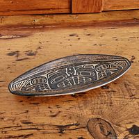 Top angled view of shallow elongated pottery dish featuring black etched Haida beaver design on dark brown ceramic.