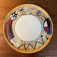 Top view of round decorative plate with abstract, colorful designs on rim and white center.
