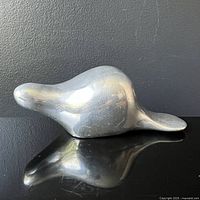 Side view image of a sleek stylized metal beaver figurine showing smooth, curved form and wear scuffs on surface.