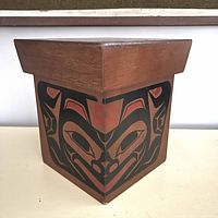 Front corner view of the wooden bentwood box displaying the bear motif in red and black paint.